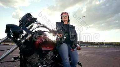 穿着皮夹克和手套坐在他酷酷的摩托车上的比基尼老妇人。 那个女人戴着<strong>圆眼镜</strong>，戴着红色的